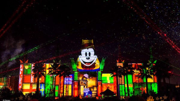Mickey Mouse and festive patterns light up a Disney World building as lasers and stars dazzle the night at Jingle Bell Jingle BAM.