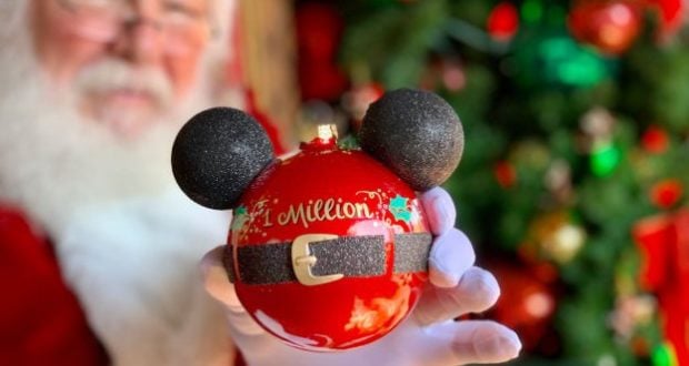 Santa celebrates 1 million guests, holding a red Mickey ornament in front of a glittering tree on Disney Springs’ Tree Trail.