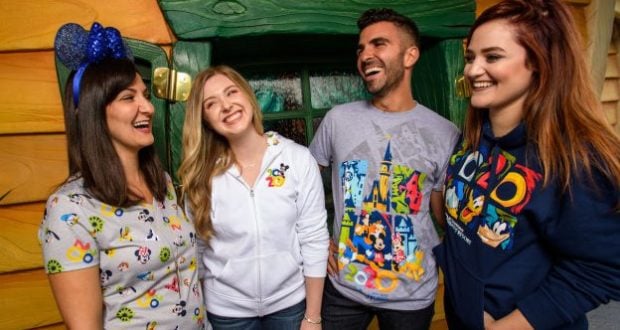 A group of friends in Disney Parks apparel laugh together outside Mickey’s Toontown house, surrounded by vibrant colors.