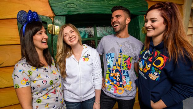 A group of friends in Disney Parks apparel laugh together outside Mickey’s Toontown house, surrounded by vibrant colors.