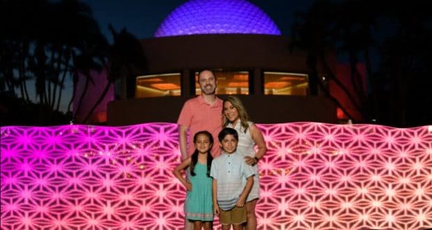 Guests pose together in front of Spaceship Earth glowing purple and pink, celebrating 15 years with a Disney PhotoPass special shot.