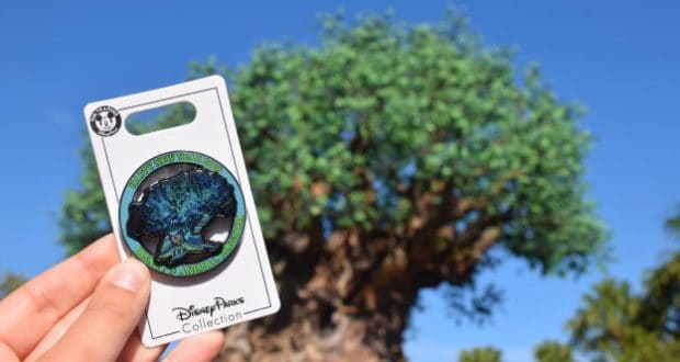 A Disney fan displays a 2020 Tree of Life pin, with the iconic Animal Kingdom tree visible softly in the background.