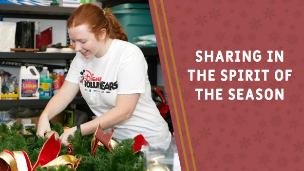 A cheerful Disney Cast Member adds festive touches to a holiday wreath near the words, "Sharing in the spirit of the season.