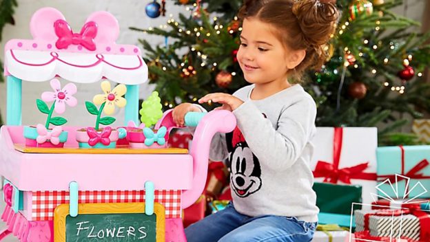 A happy child enjoys a shopDisney pink flower stand toy near a sparkling Christmas tree and festive Disney holiday presents.