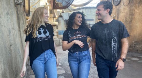 Fans sporting Star Wars shirts laugh together outside, proudly displaying exclusive Rise of the Resistance gear at Disney Parks.