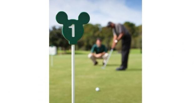 Mickey Mouse–themed green golf marker marked “1” on a Disney World course, with two golfers putting in the background.