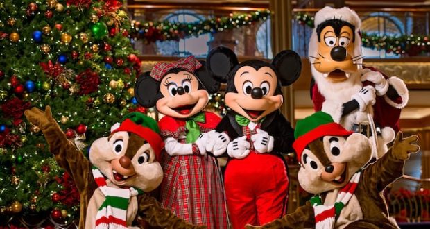 Mickey, Minnie, Goofy, Donald, and Pluto in Christmas costumes gather by a twinkling tree aboard Disney Cruise Line.