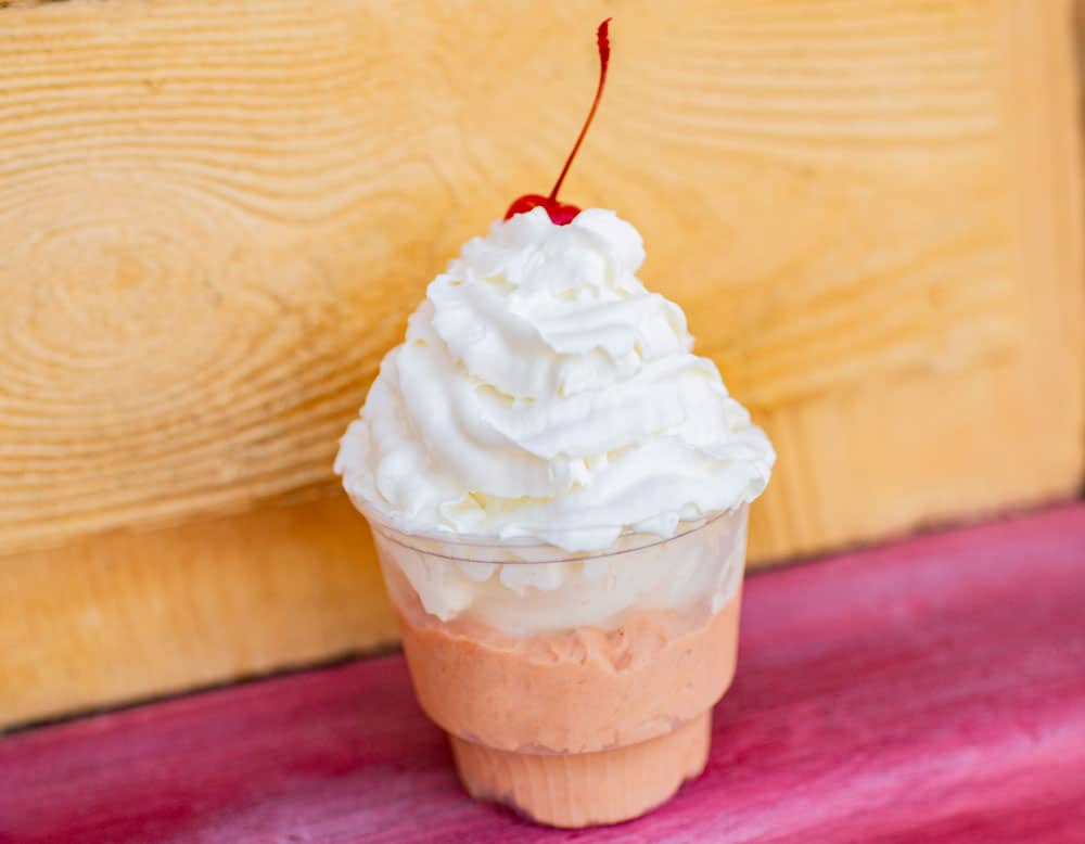 Disney’s Typhoon Lagoon-inspired orange and vanilla soft serve topped with whipped cream and a cherry, pops against vibrant park colors.
