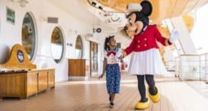 A child beams while holding hands with Sail Away Minnie on the deck of a Disney Cruise Line ship, ready for magical adventures.