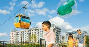 Young guest with a balloon strolls by Disney Skyliner and resort towers, enjoying the sunny excitement of Walt Disney World.