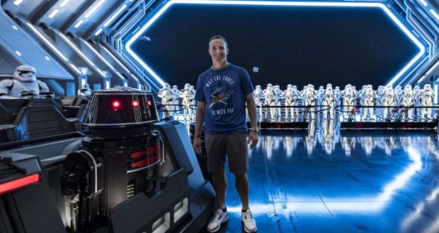 A guest strikes a confident pose at Star Wars: Galaxy’s Edge, with stormtroopers and a droid adding to the immersive scene.