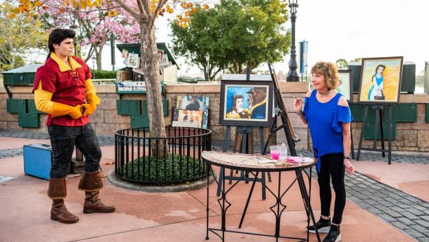 At Epcot's Festival of the Arts, an artist paints Disney characters while Gaston from Beauty & The Beast looks on nearby.