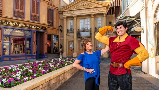 Guest smiles with Gaston, who flexes triumphantly in Belle’s Village at EPCOT’s Beauty and the Beast Sing-Along experience.