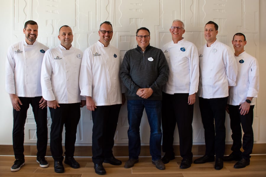 Disney Parks chefs in white coats smile together in front of a patterned wall, celebrating Appetizing Occasions in Jan 2020.