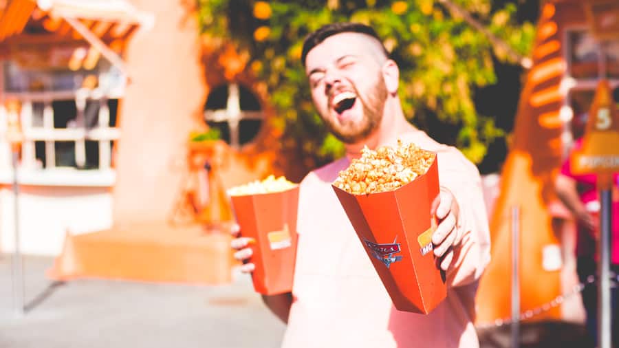 Guest grinning in the sunshine at Disney Parks, holding two jumbo popcorn buckets—ready for National Popcorn Day festivities.