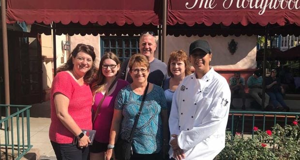 Chef and five smiling guests pose outside The Hollywood restaurant, celebrating like Disney Hero Volunteer Families at Disney parks.