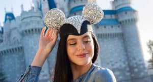 Disney fan beams in a sparkling Designer Collection Mickey Ear Hat, posing before the iconic castle at a Disney park.