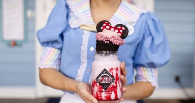 Enjoying a colorful pink milkshake topped with a Minnie Mouse cupcake and candy at Beaches & Cream Soda Shop in Disney World.