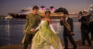 Tiana in her green gown and Prince Naveen greet guests riverside as live jazz plays, with Disney Wonder docked in New Orleans.