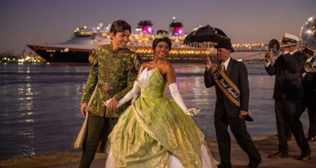 Tiana in her green gown and Prince Naveen greet guests riverside as live jazz plays, with Disney Wonder docked in New Orleans.