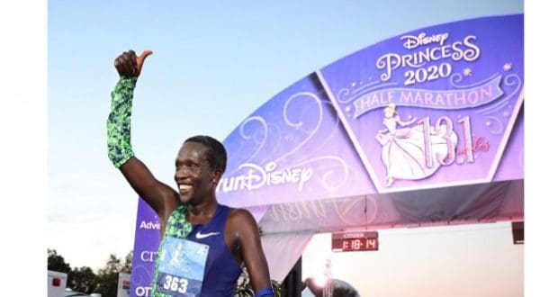 A determined double amputee runner celebrates with a thumbs up at the Disney Princess Half Marathon finish line in 2020.
