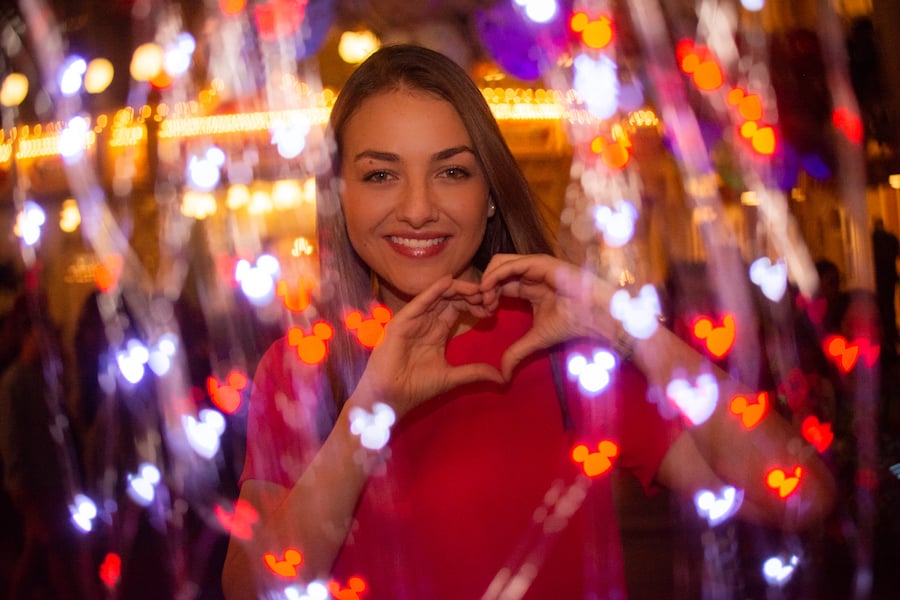 A guest in red makes a heart with her hands, surrounded by glowing Mickey lights—feel the Disney World magic all around!.