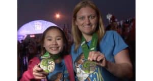 Two Disney fans in matching blue shirts beam as they show off their Princess 5K medals at a magical runDisney event.