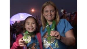 Two Disney fans in matching blue shirts beam as they show off their Princess 5K medals at a magical runDisney event.
