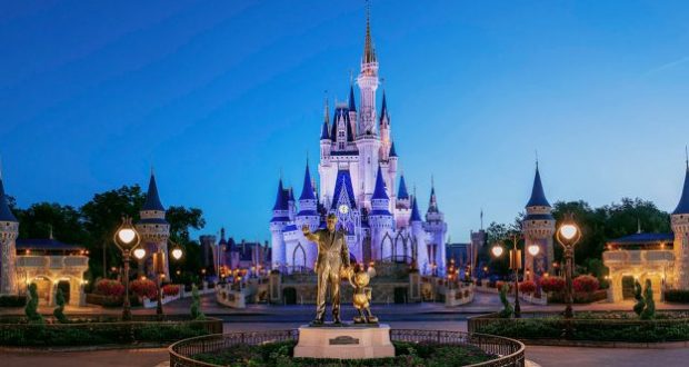 Cinderella Castle glowing at dusk in Disney World with Walt Disney and Mickey Mouse's statue, capturing classic park magic.