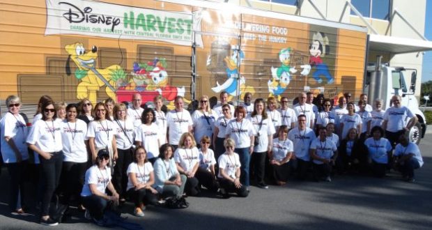 Disney Cast Members in matching shirts gather by the Disney Harvest truck, featuring classic characters and supporting Second Harvest.