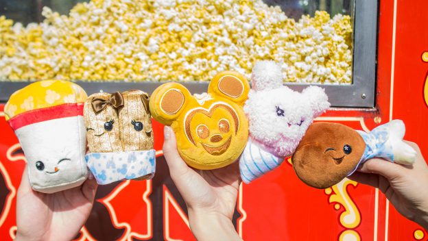 Wishables plushes—popcorn, churros, Mickey Mouse, bunny, turkey leg—held at Disney Parks with popcorn piles in the background.