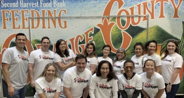 Disneyland Resort volunteers in matching shirts smile by a "Feeding Orange County" food bank sign, celebrating their charitable success.