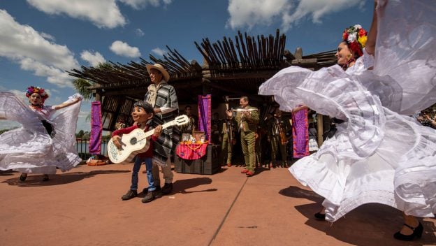 Mariachi Cobre brings Coco’s story to life at EPCOT, performing in vibrant Mexican attire under the sunny festival sky.