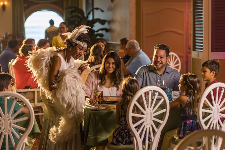 A costumed performer delights a family at a vibrant New Orleans-style restaurant as guests revel in the festive, immersive atmosphere.