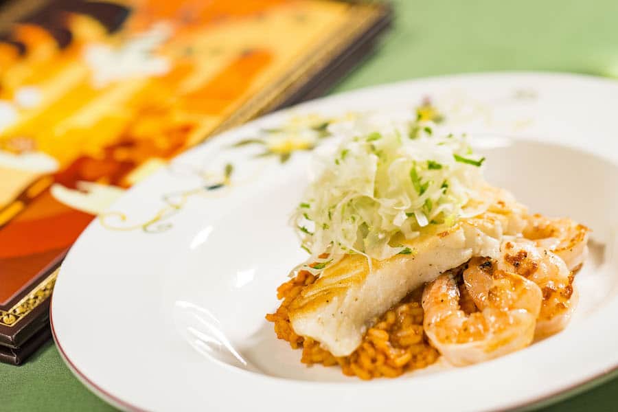 Seafood rice bowl with shrimp, fish, and greens beside a vibrant Disney Wonder New Orleans-inspired cruise menu.