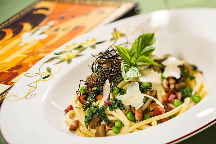 Bucatini pasta with peas, greens, pancetta, cheese shavings, and basil on a festive plate—New Orleans flavors at Disney Springs.