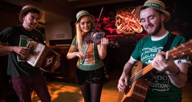 Musicians in festive hats perform guitar, violin, and accordion on Raglan Road’s warmly lit stage for the St. Patrick’s Festival.