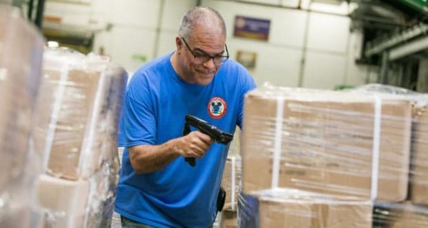 Cast member in a blue shirt scans boxes with a barcode scanner backstage, prepping supplies for attractions at the park.