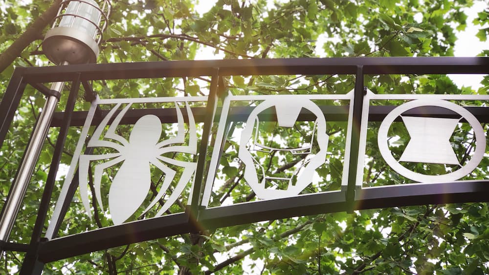 Spider-Man, Iron Man, and Black Widow symbols on a Marvel gate with trees behind—ideal for National Super Hero Day at the park.