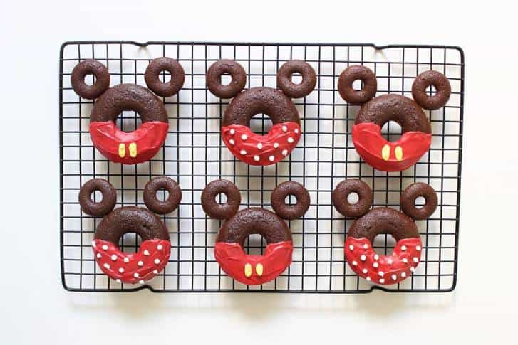 Minnie Mouse-inspired chocolate donuts with red bows and polka dots on a rack—perfect for Disney Parks snack fans!.