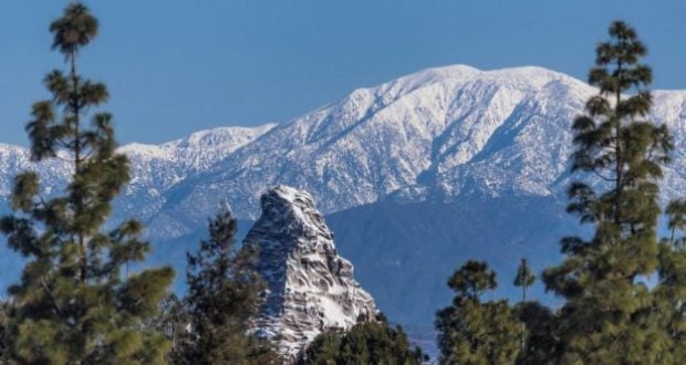 The Matterhorn’s snow-capped peaks tower above lush green trees and a bright blue sky, just like at Disneyland’s Fantasyland.