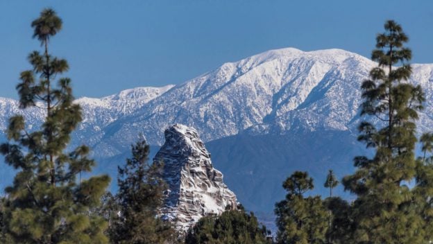 The Matterhorn’s snow-capped peaks tower above lush green trees and a bright blue sky, just like at Disneyland’s Fantasyland.