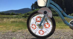 Blue bike’s front wheel decorated with Star Wars paper crafts, featuring BB-8, shines under sunny skies with mountain views.