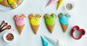 Mickey Ice Cream Cone Cookies with colorful icing and sprinkles, surrounded by baking gear for a Disney-inspired treat at home.
