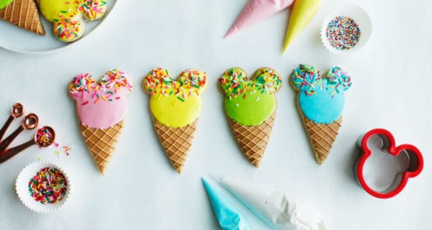 Mickey Ice Cream Cone Cookies with colorful icing and sprinkles, surrounded by baking gear for a Disney-inspired treat at home.