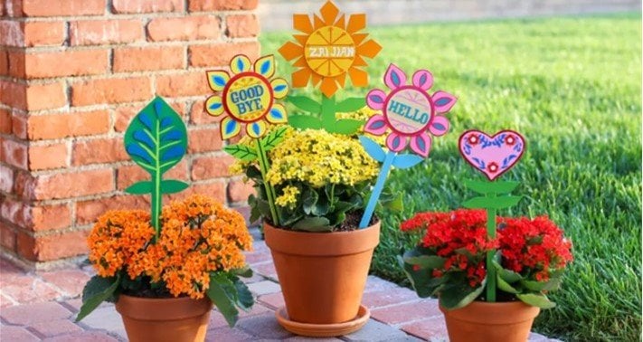 Colorful flower pots with “GOOD BYE,” “HELLO,” and cheerful DIY stakes evoke the whimsy of it’s a small world at Disney Parks.