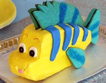 Flounder cake inspired by Ariel, with yellow icing, blue stripes, big eyes, and cookie fins—perfect for Disney fans at home.