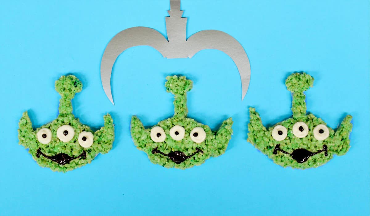 Green alien Rice Crispy Treats under a silver claw on Toy Story Land-inspired blue, evoking the iconic Pixar attraction.