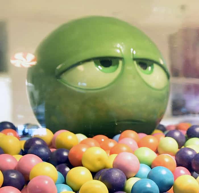 A giant green gumball with a bored face peeks from a candy display onboard Disney Cruise Line—find this playful detail at sea!.