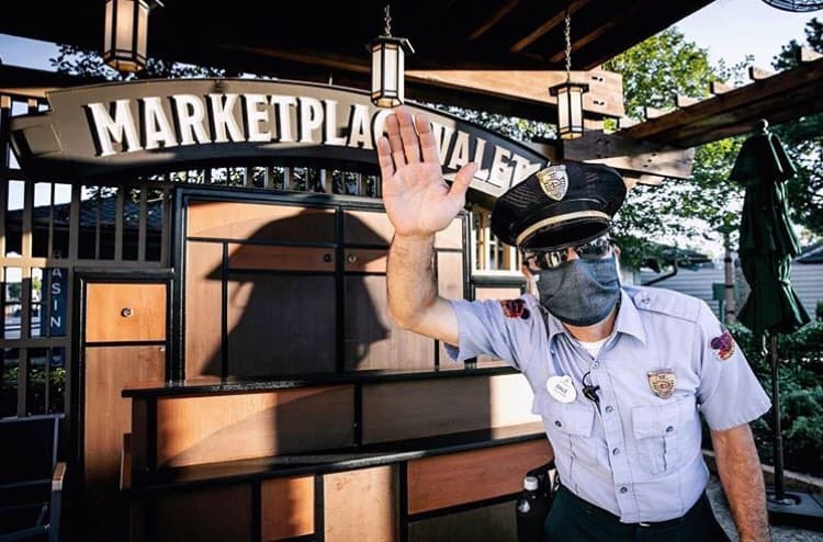 A Marketplace Valet team member waves in uniform and mask, ready to welcome guests arriving at Disney Springs.